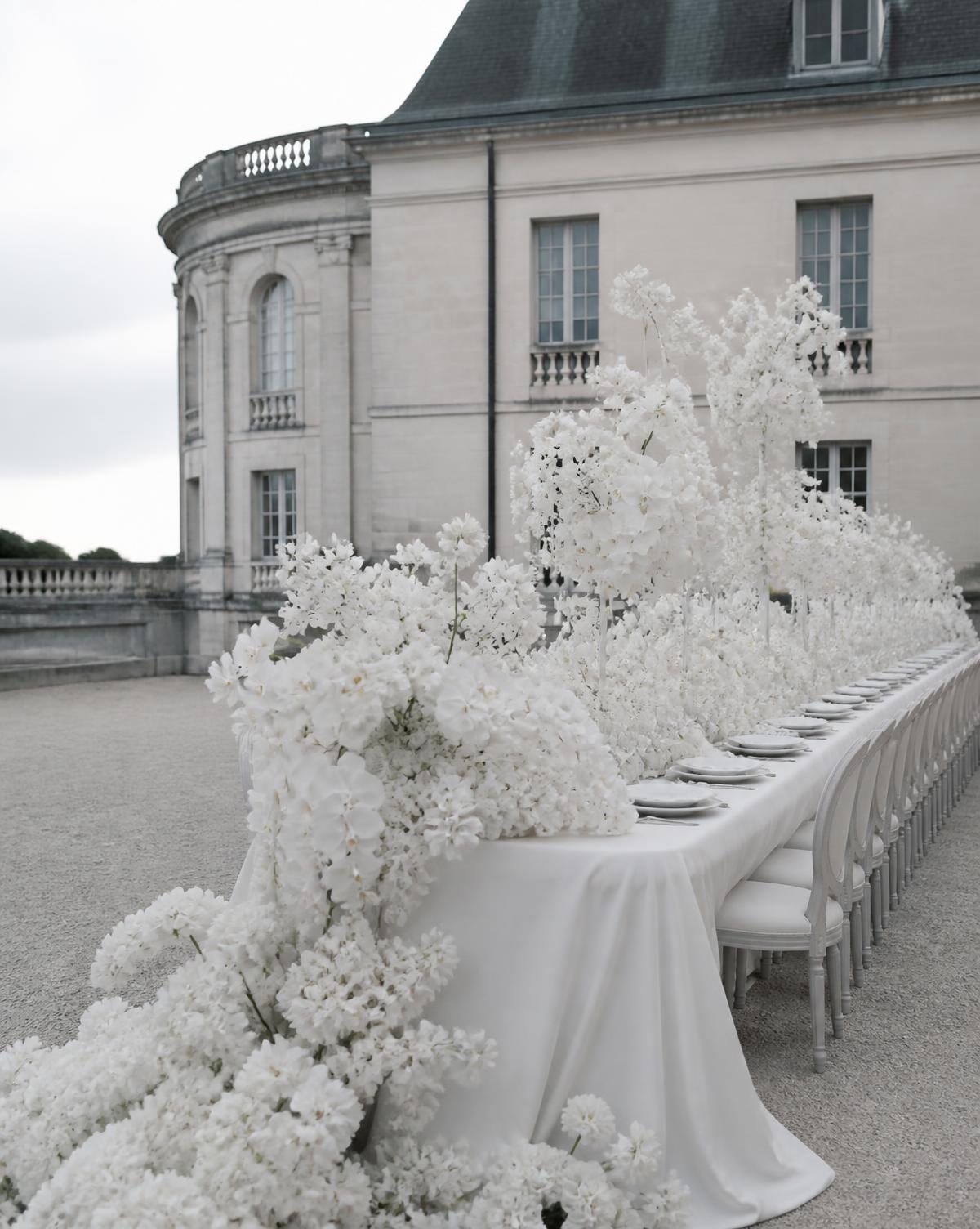 Long table surrounded by sculptural white wedding flowers at a European estate